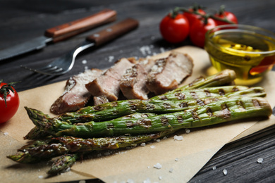 Photo of Tasty meat served with grilled asparagus on parchment, closeup