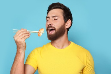 Photo of Handsome man eating sushi with chopsticks on light blue background