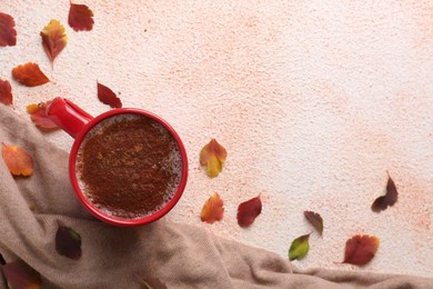 Cup of hot drink, leaves and soft knitted fabric on beige textured table, flat lay with space for text. Cozy autumn atmosphere