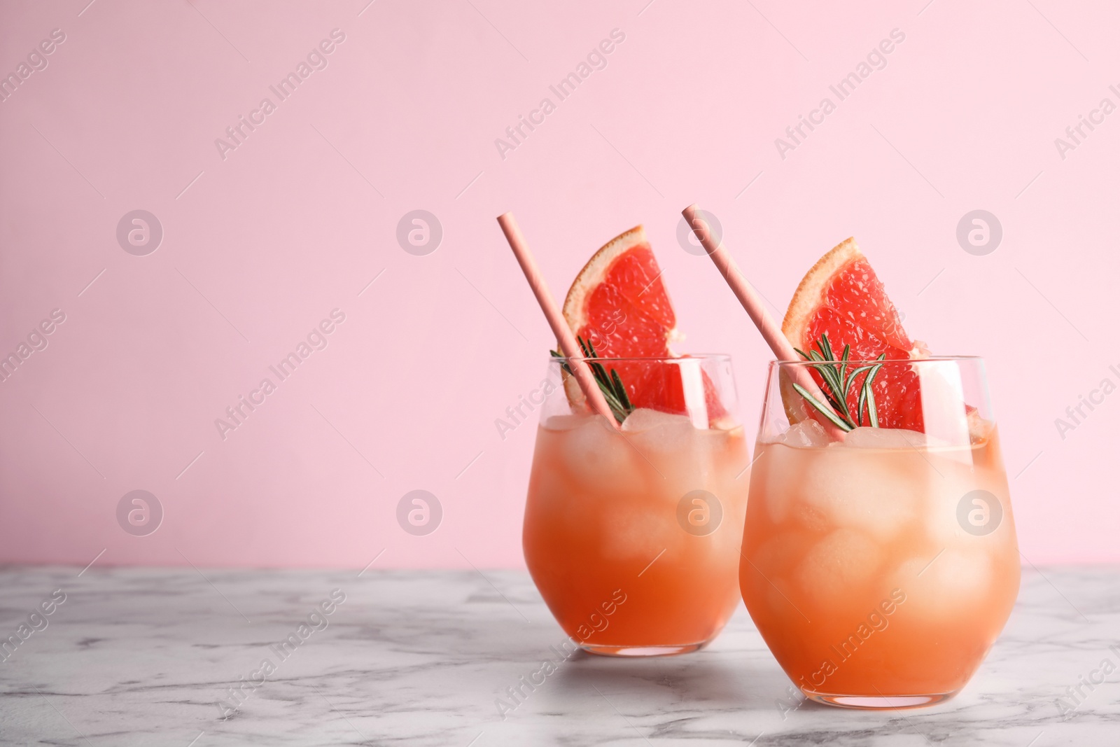 Photo of Glasses of grapefruit cocktails on table against color background. Space for text