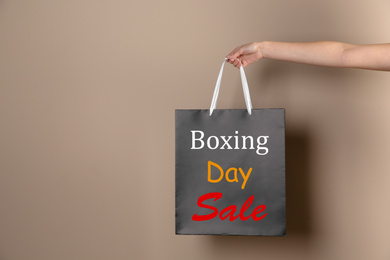 Image of Boxing day sale. Woman holding shopping bag on beige background, space for text