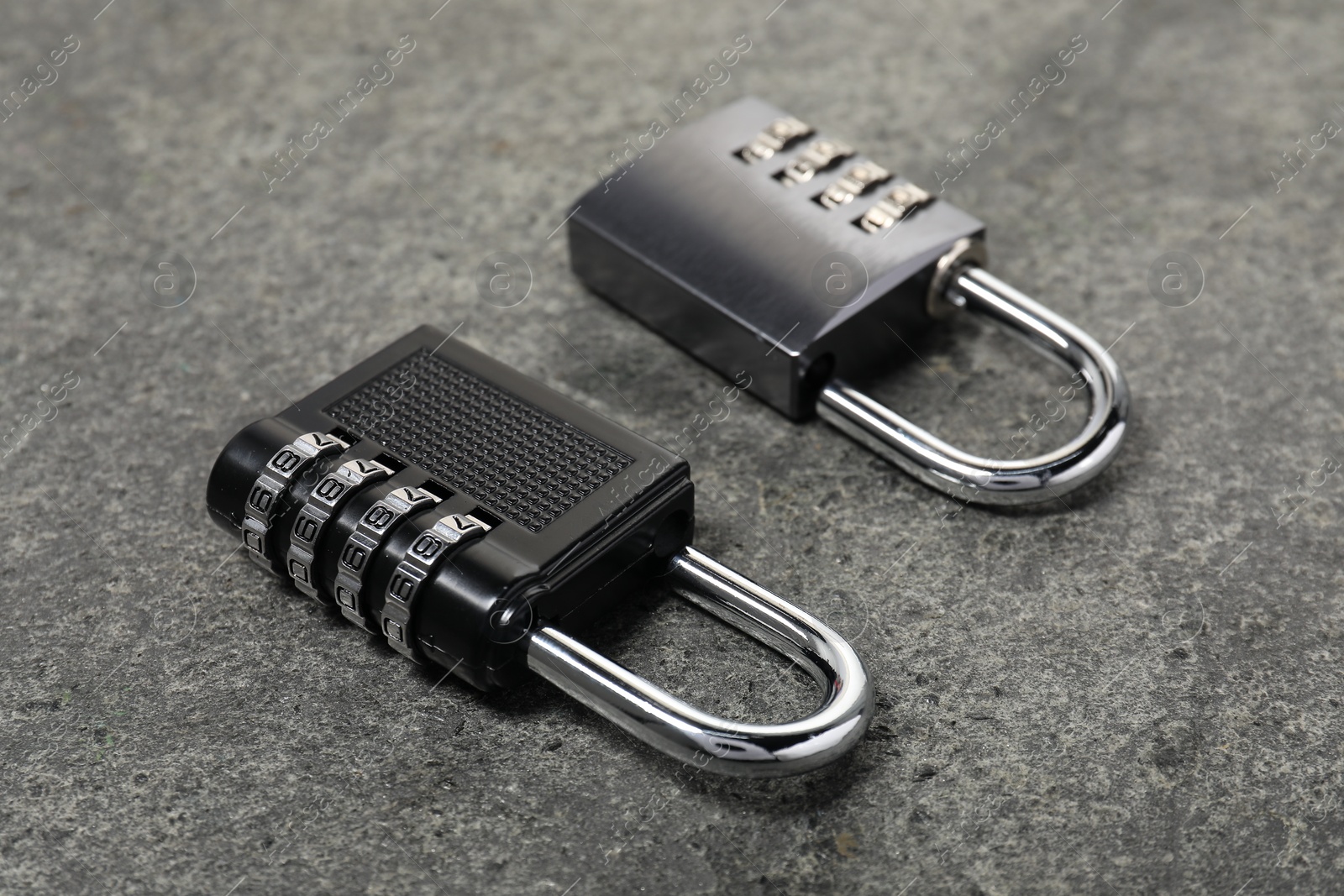 Photo of Locked steel combination padlocks on grey stone table, closeup