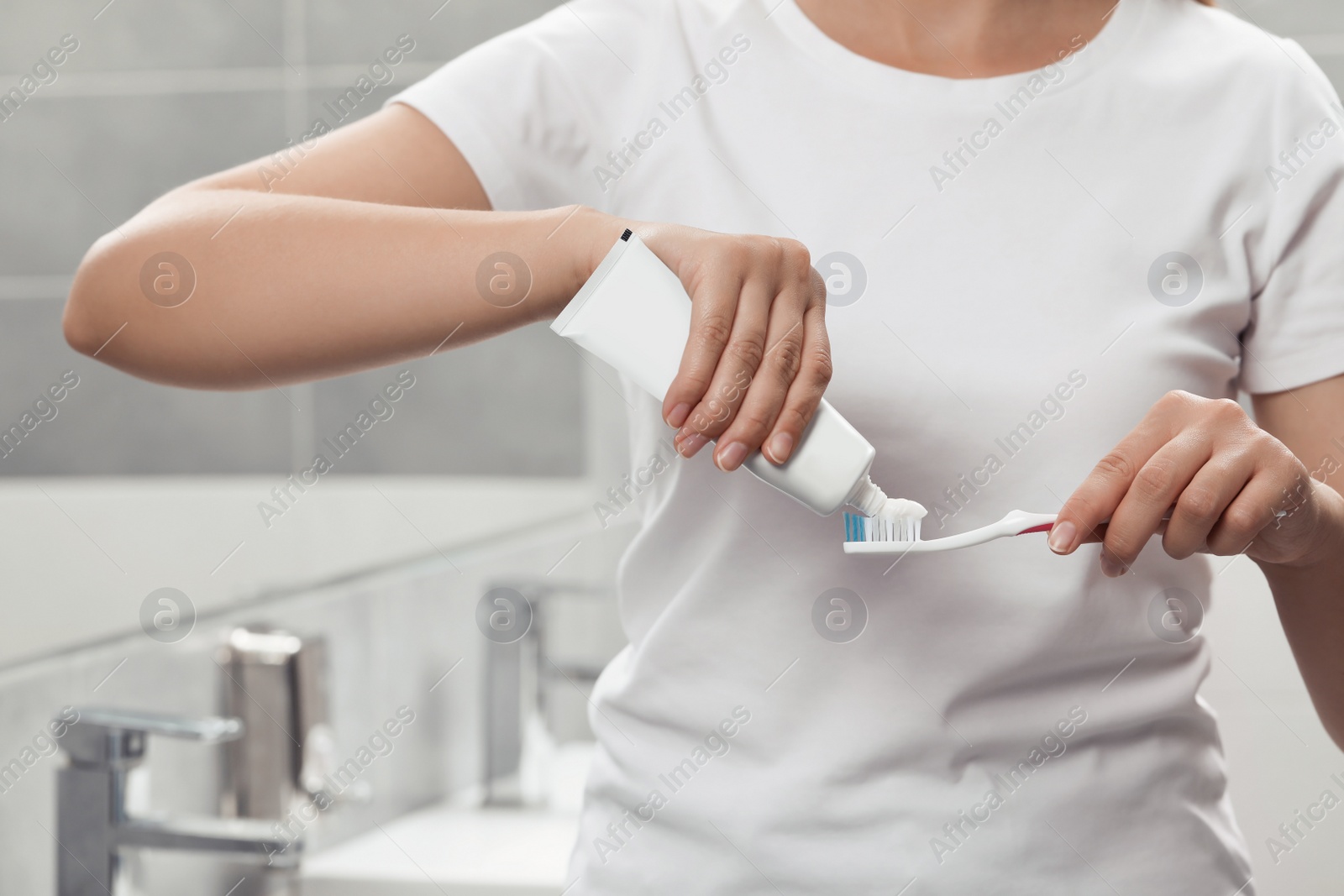 Photo of Woman applying toothpaste on brush in bathroom, closeup