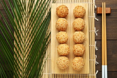 Photo of Delicious sesame balls, green leaf, chopsticks on wooden table, flat lay