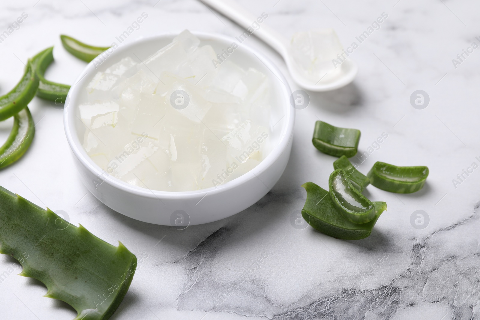 Photo of Aloe vera gel and slices of plant on white marble table, closeup