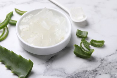 Aloe vera gel and slices of plant on white marble table, closeup