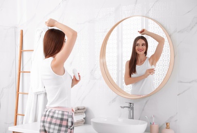 Beautiful young woman applying deodorant in bathroom