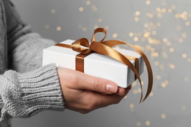 Christmas present. Woman holding gift box against grey background with blurred lights, closeup