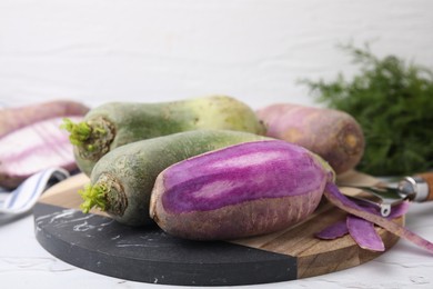 Photo of Purple and green daikon radishes on white textured table, closeup