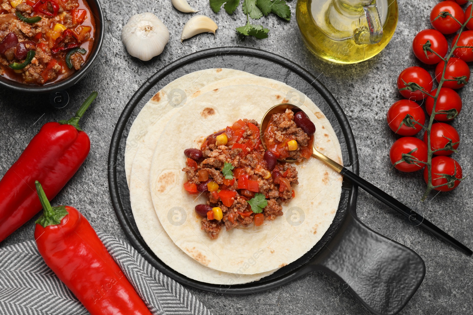 Photo of Tasty chili con carne with tortilla and ingredients on grey table, flat lay