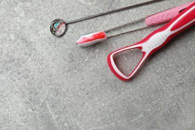 Photo of Red tongue cleaner, dentist mirror and toothbrush with paste on grey background. Space for text