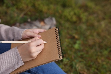 Young woman drawing with pencil in sketchbook outdoors, closeup. Space for text