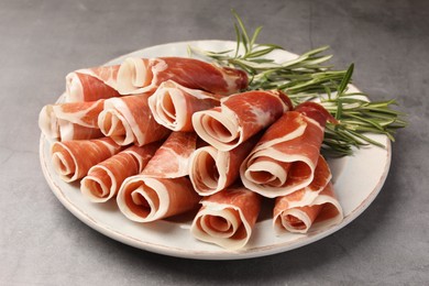 Photo of Rolled slices of delicious jamon with rosemary on grey table