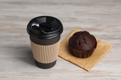 Paper cup with black lid and muffin on wooden table. Coffee to go