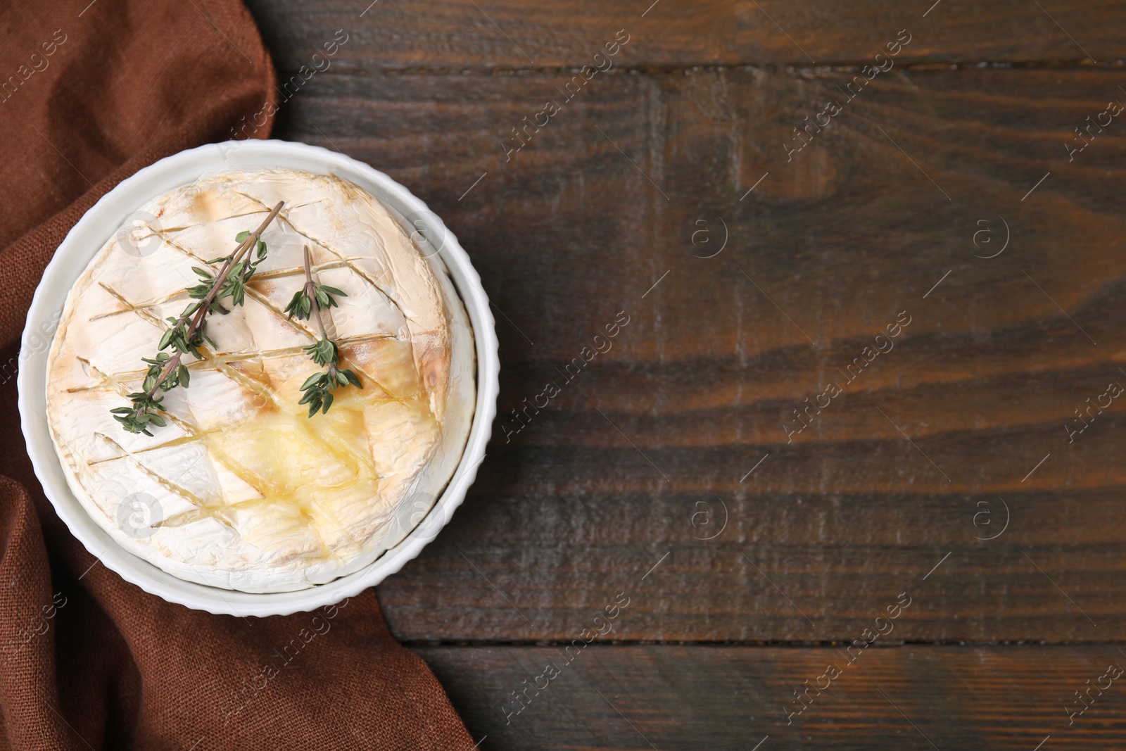 Photo of Tasty baked camembert and thyme in bowl on wooden table, top view. Space for text