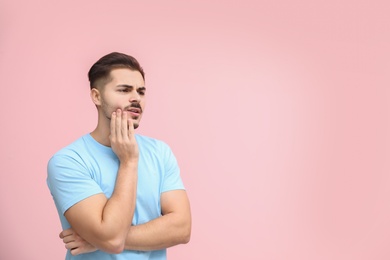 Young man suffering from strong tooth pain on color background, space for text