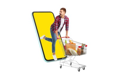 Grocery shopping via internet. Excited man with shopping cart full of products running out of huge smartphone on white background