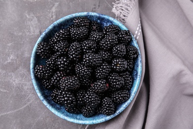 Photo of Bowl of ripe blackberries and fabric on grey table, flat lay