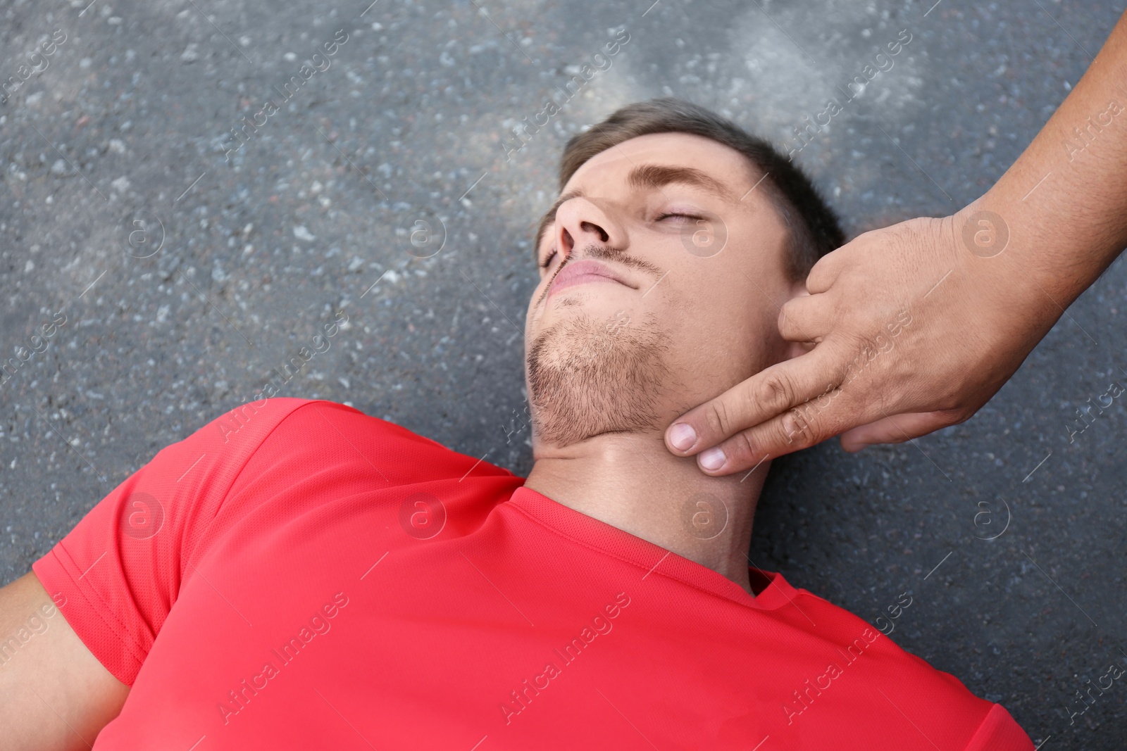 Photo of Passerby checking pulse of unconscious young man outdoors