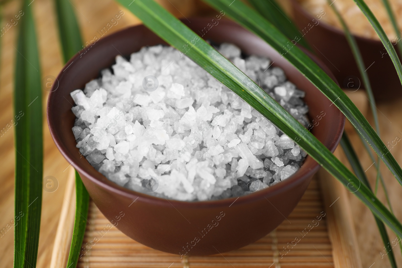 Photo of Salt for spa scrubbing procedure and leaves on wooden table, closeup
