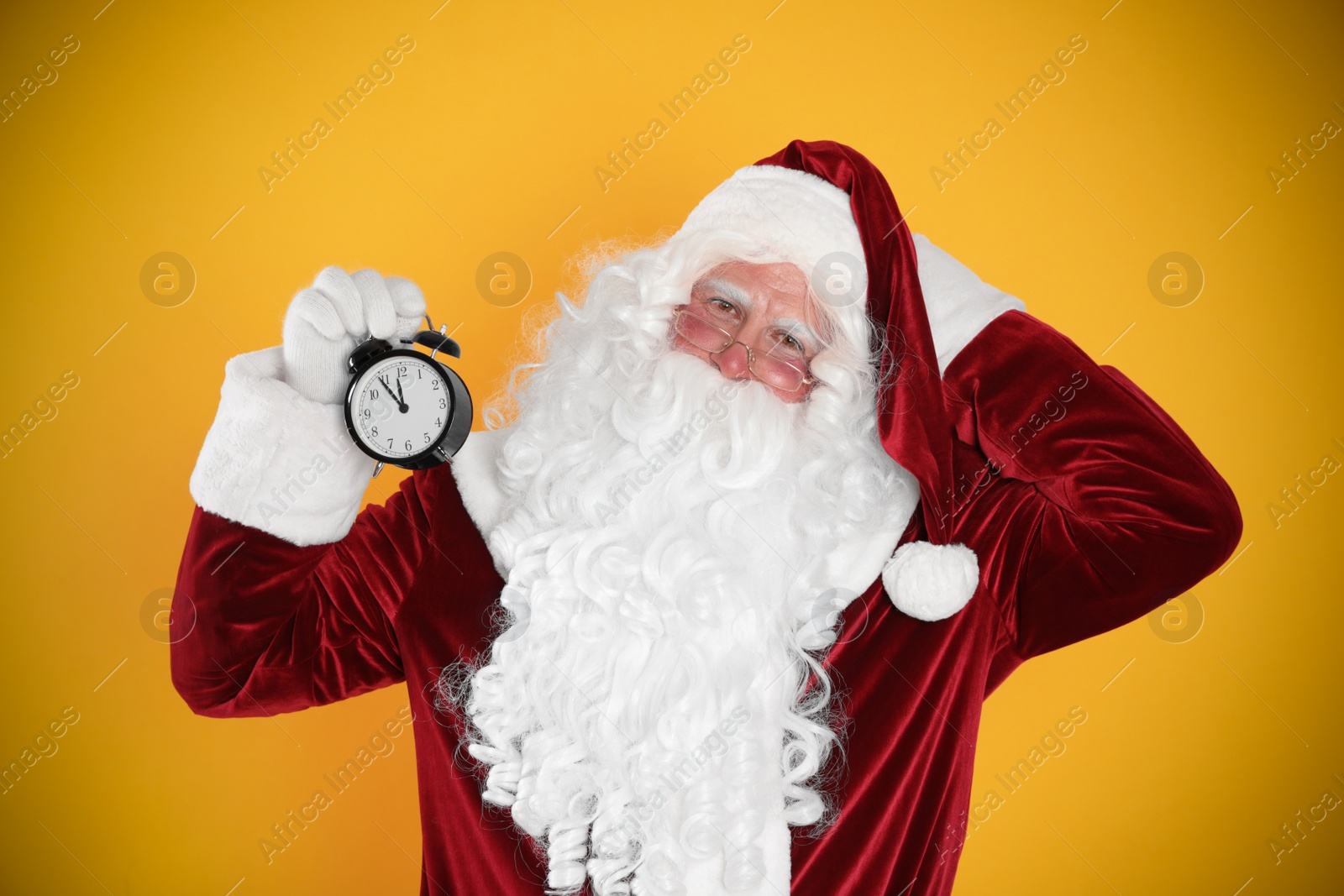 Photo of Santa Claus holding alarm clock on yellow background. Christmas countdown