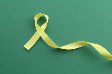 Yellow awareness ribbon on green background, top view