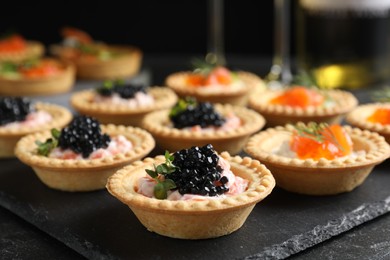 Photo of Delicious canapes with salmon and caviar on black table, closeup