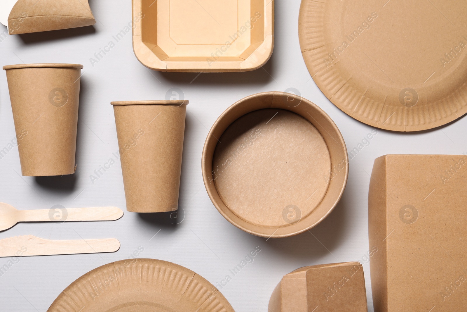 Photo of Eco friendly food packaging. Paper containers and tableware on light grey background, flat lay