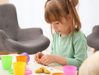 Photo of Cute little girl using play dough at table indoors