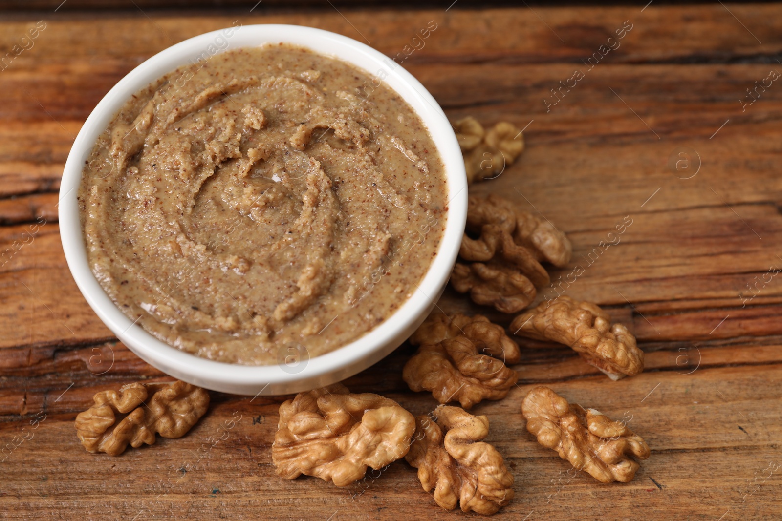 Photo of Delicious nut butter in bowl and walnuts on wooden table, closeup