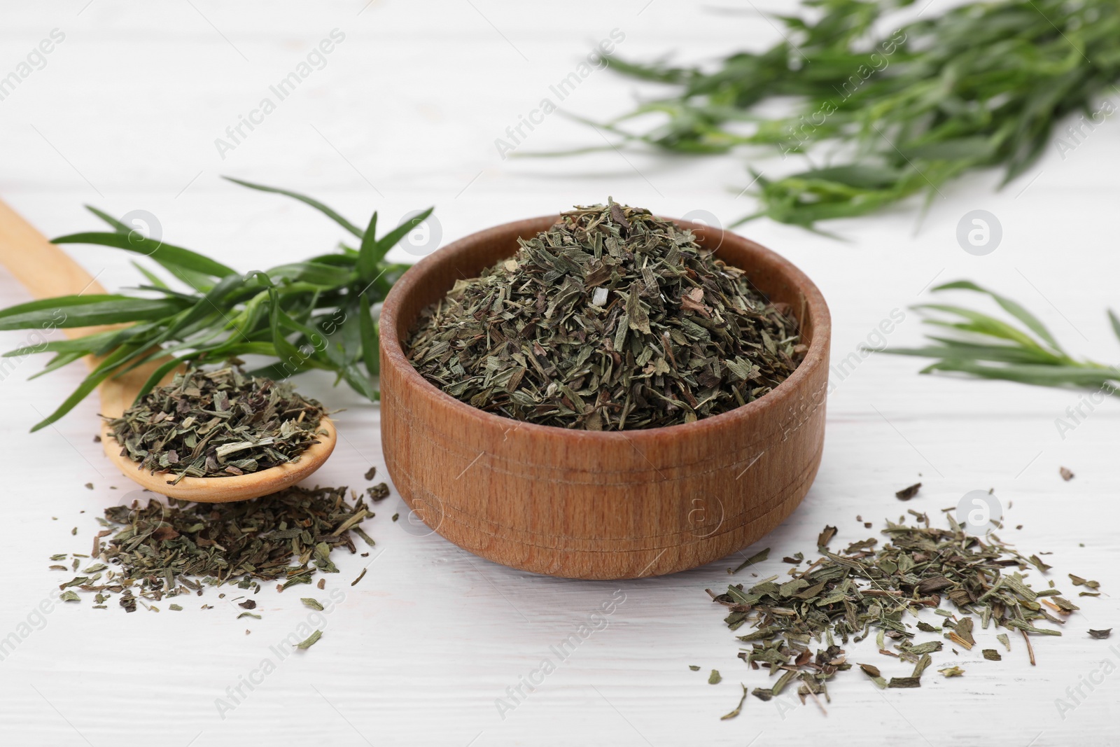 Photo of Bowl of dry tarragon, spoon and fresh leaves on white wooden table