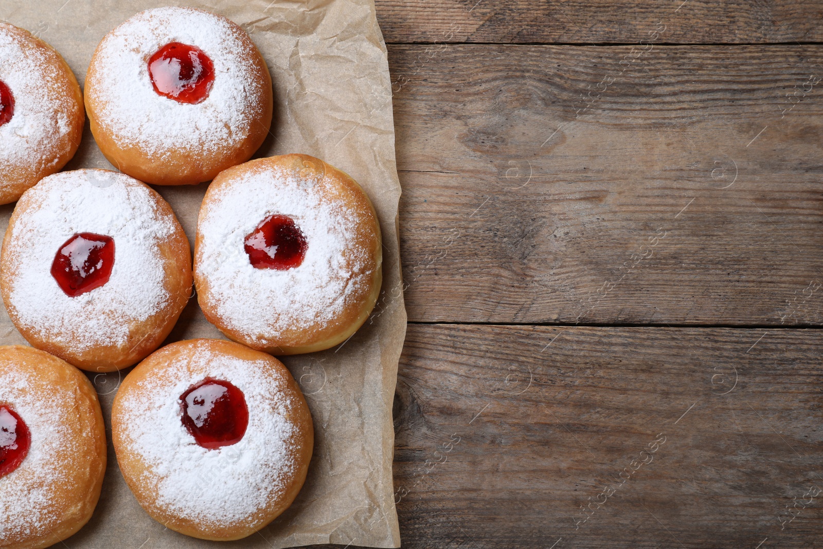 Photo of Hanukkah doughnuts with jelly and sugar powder on wooden table, flat lay. Space for text