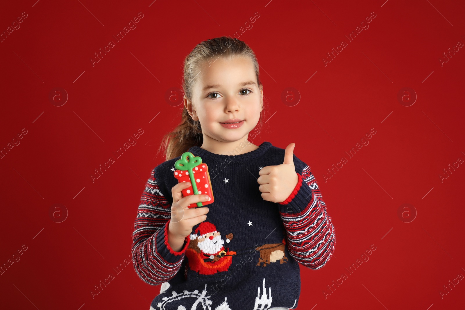 Photo of Cute little girl with Christmas gingerbread cookie on red background