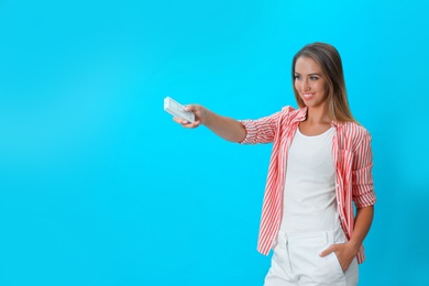 Photo of Young woman with air conditioner remote on blue background. Space for text