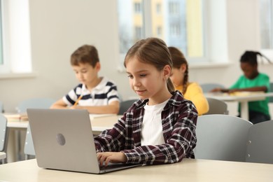 Photo of Cute little girl with laptop studying in classroom at school