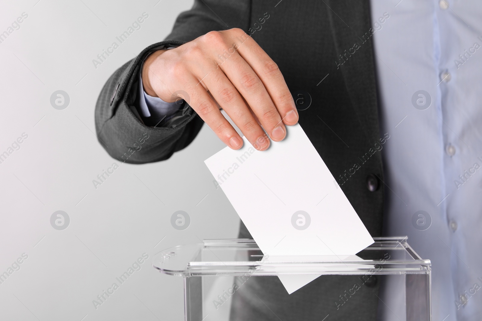 Photo of Man putting his vote into ballot box on light grey background, closeup