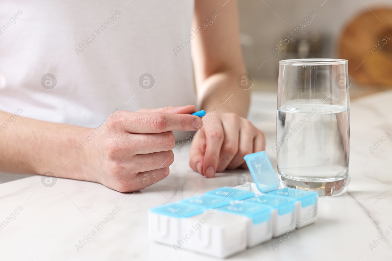 Photo of Woman with pills, organizer and glass of water at white marble table, closeup