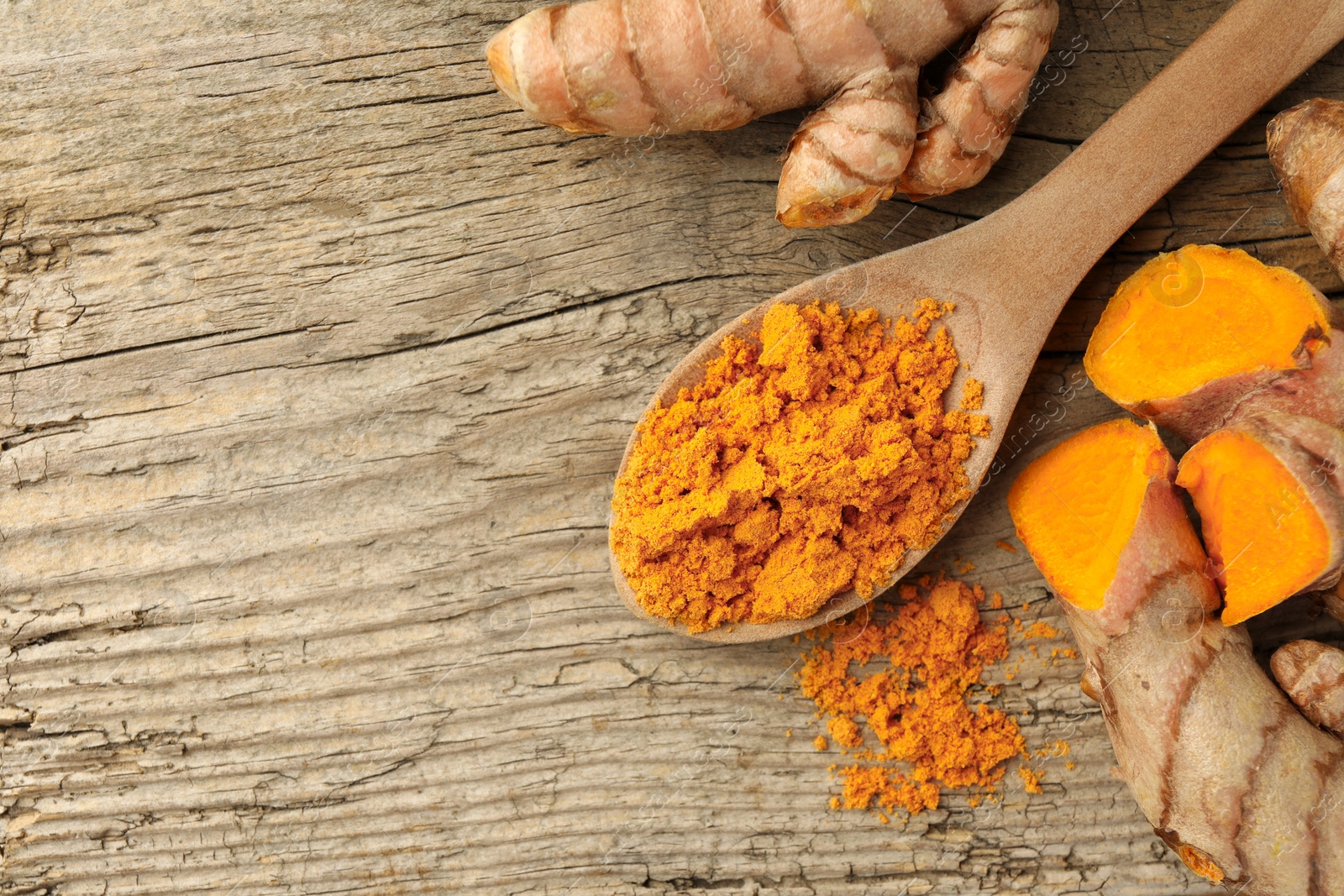 Photo of Aromatic turmeric powder and raw roots on wooden table, flat lay. Space for text