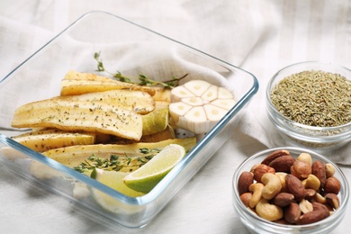 Photo of Raw cut white carrot with lime slices and garlic in baking dish on wooden table