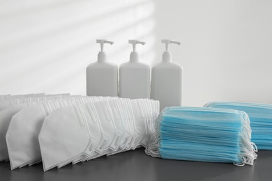 Photo of Hand sanitizers and respiratory masks on grey table indoors. Protective essentials during COVID-19 pandemic