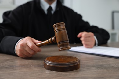 Photo of Judge with gavel and papers sitting at wooden table indoors, closeup