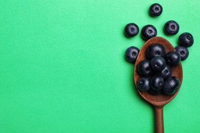 Photo of Fresh acai berries with wooden spoon on green background, flat lay. Space for text