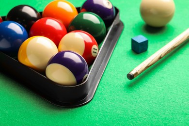 Photo of Billiard balls in triangle rack, cue and chalk on green table, closeup