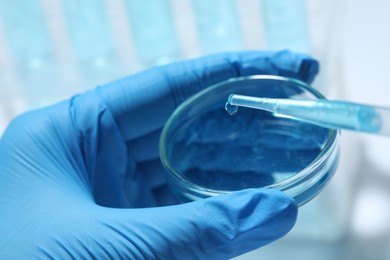 Photo of Scientist dripping liquid from pipette into petri dish on light background, closeup