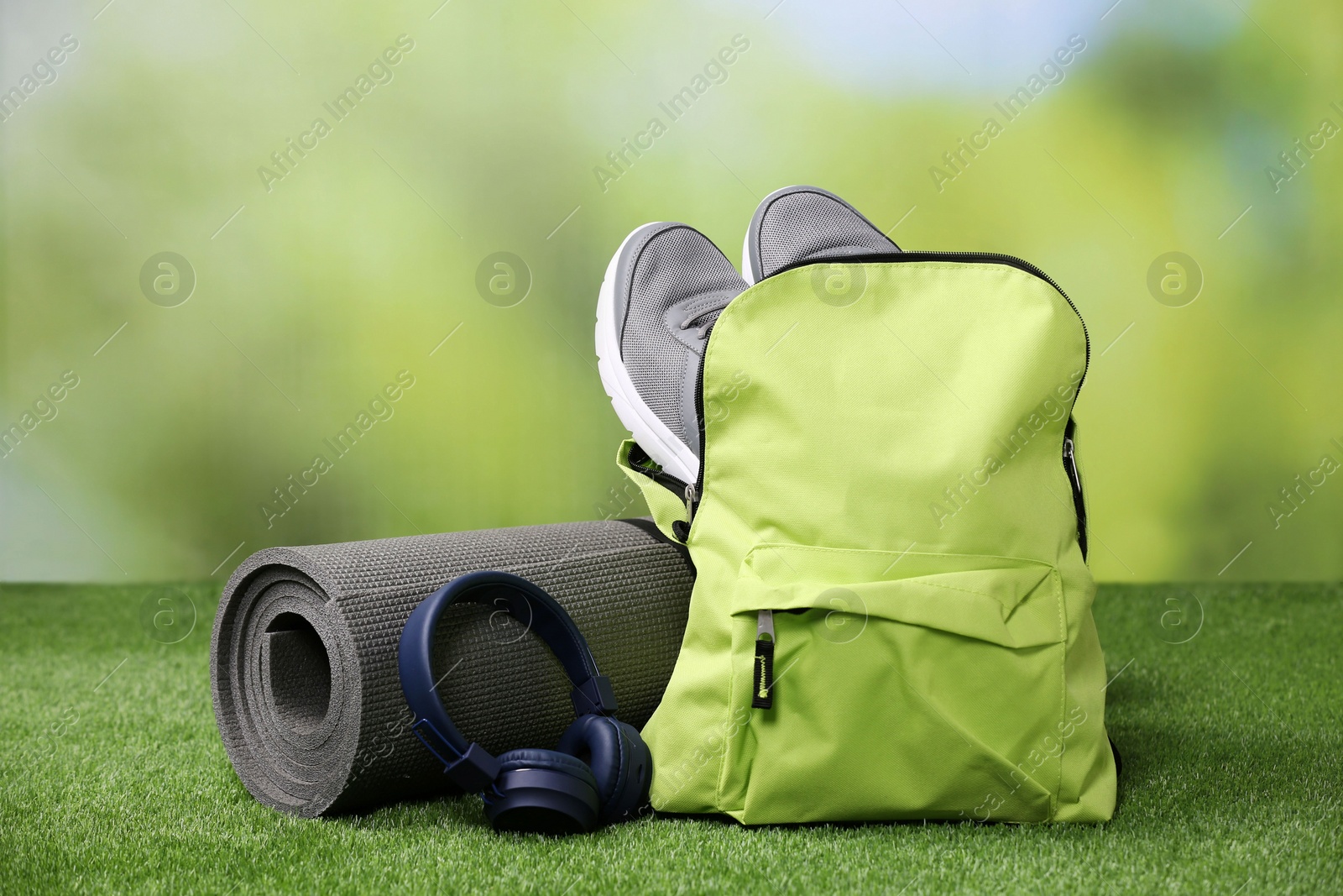 Photo of Backpack and different sports equipment on grass against blurred background