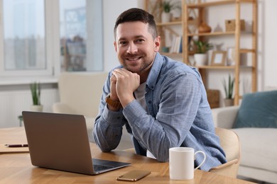 Happy man working on laptop at wooden desk in room