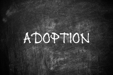 Image of Word ADOPT written with chalk on blackboard, top view. Family concept