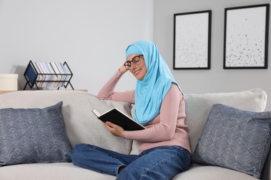 Muslim woman reading book on couch in room