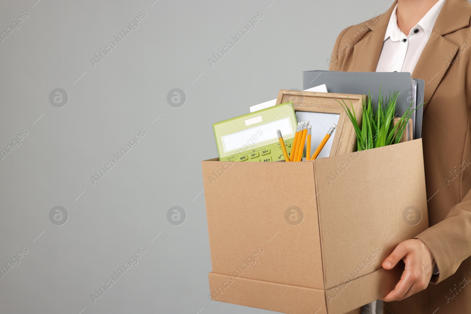 Photo of Unemployed woman holding box with personal office belongings on grey background, closeup. Space for text