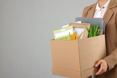 Photo of Unemployed woman holding box with personal office belongings on grey background, closeup. Space for text